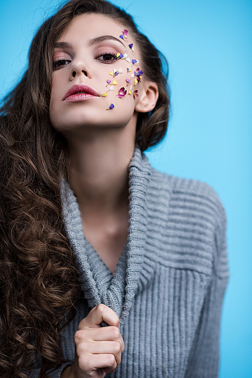 young woman in stylish turtleneck sweater with flowers on face isolated on blue