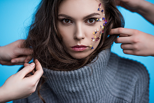 stylists working with model in turtleneck sweater with flowers on face