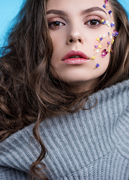 close-up portrait of woman in warm grey sweater with flowers attached to face