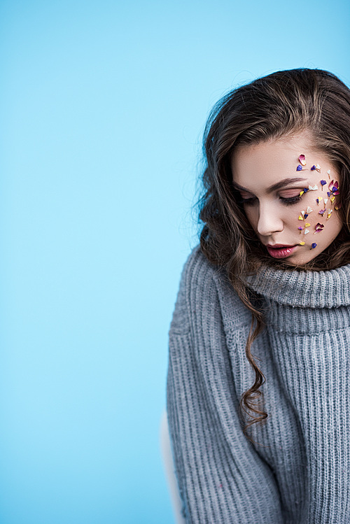 beautiful woman in warm grey sweater and flowers on face isolated on blue