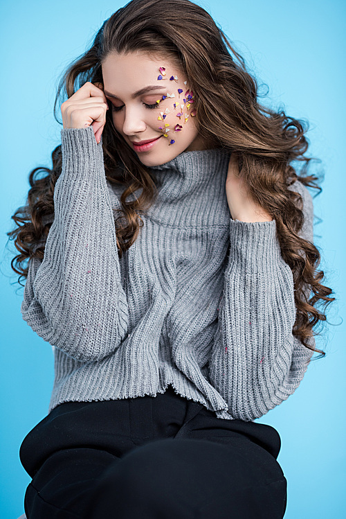 beautiful smiling brunette woman with flowers on face and closed eyes posing isolated on blue