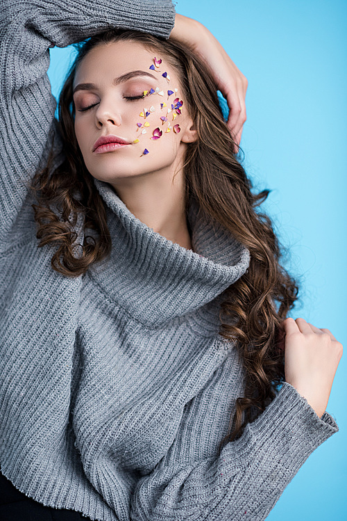 sensual young woman with closed eyes and flowers on face posing isolated on blue