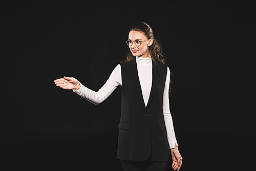 beautiful brunette woman in eyeglasses pointing away isolated on black