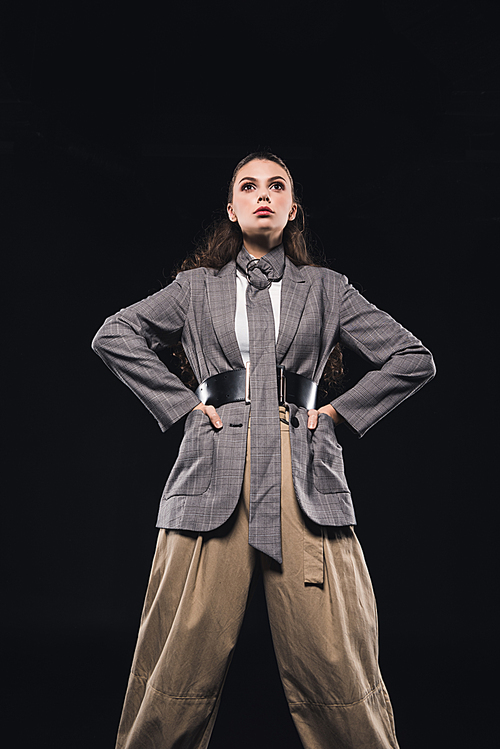 low angle view of confident young woman with hands on waist posing isolated on black