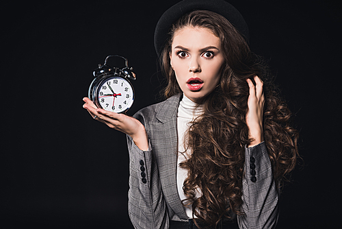 shocked young woman holding clock and  isolated on black