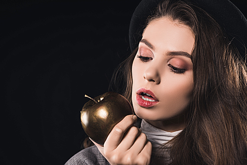 beautiful fashionable young woman eating golden apple isolated on black