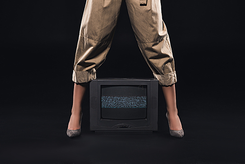 low section of stylish woman standing with tv with noises on the screen on black