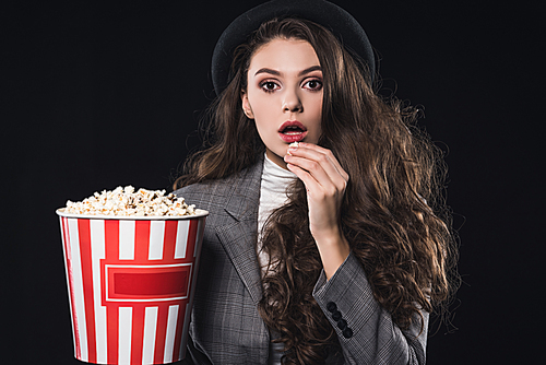 shocked fashionable young woman eating popcorn and  isolated on black