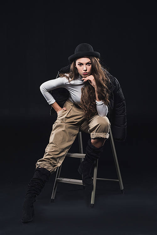 beautiful young woman in fashionable hat and winter jacket sitting on ladder and  on black