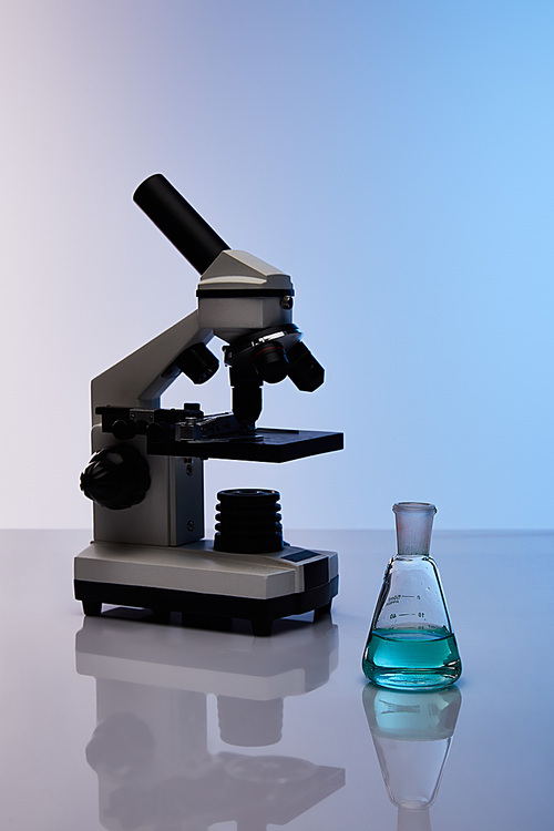 glass flask with colorful blue liquid near microscope