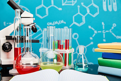 microscope, glass test tubes and flasks with colorful liquid near copybook and books on blue background with molecular structure