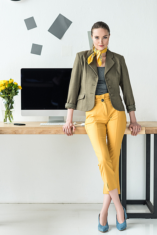 beautiful businesswoman in fashionable clothing leaning on workplace with computer screen in office