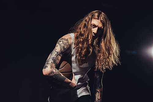 tattooed man with long hair playing basketball, isolated on black