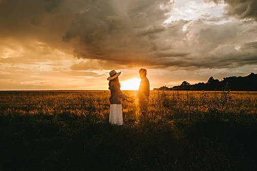 young couple holding hands on meadow at sunset with backlit, love story