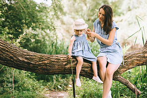 mom and daughter sitting on tree and spending time together in nature