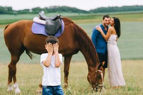 parents hugging and son covering eyes on foreground on field