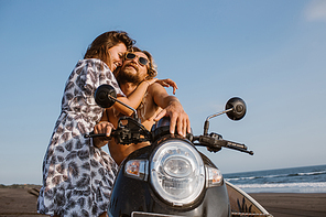 girlfriend cuddling boyfriend on scooter at beach in bali, indonesia