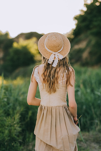 back view of blonde girl in elegant dress and straw hat