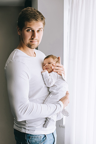 portrait of father carrying little baby boy in front of curtains at home