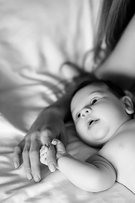 black and white picture of mother holding hand of little baby boy in bed at home