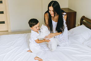 beautiful young mother and child playing with bichon dog in bed at home