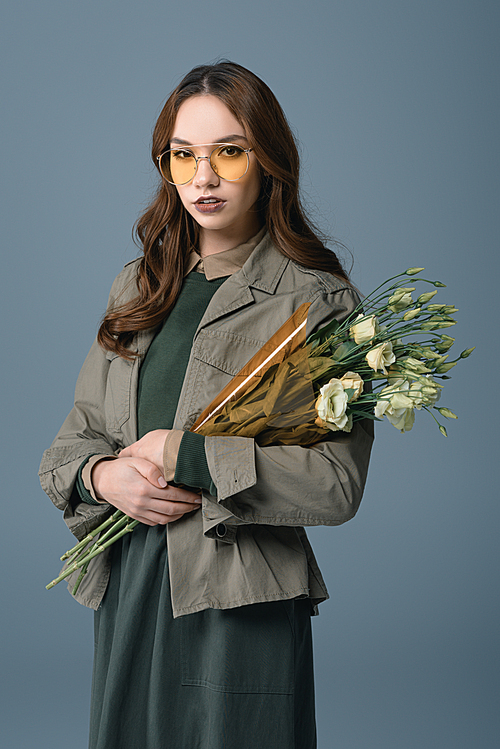 fashionable girl posing in autumn outfit with bouquet of flowers, isolated on grey