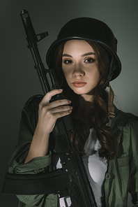 beautiful young woman in military helmet with rifle, on grey with shadows