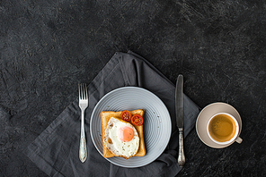 flat lay with cup of coffee and toast with fried egg and cherry tomatoes for breakfast on dark surface