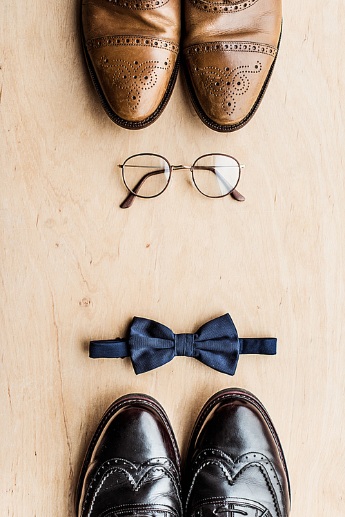 top view of shoes, glasses and tie bow on wooden surface