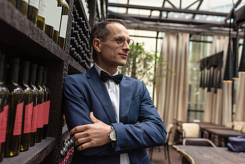 handsome man in stylish suit standing in front wine storage at restaurant