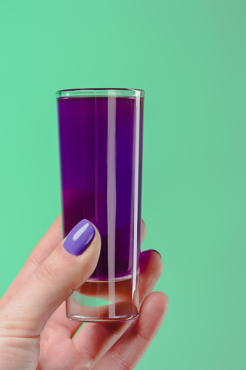cropped image of woman holding glass with purple cocktail isolated on turquoise