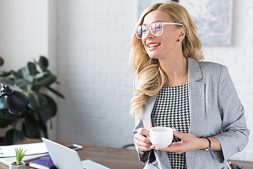 smiling businesswoman holding cup of coffee and looking away