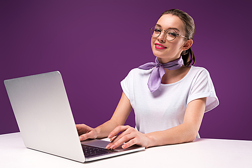 smiling girl using laptop and  isolated on purple