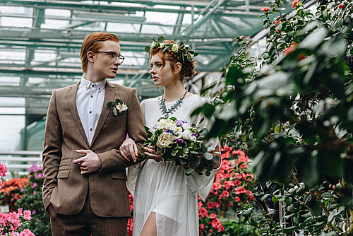 beautiful stylish young bride and groom walking together in botanical garden