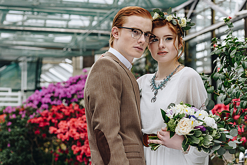 beautiful elegant young redhead wedding couple standing with bouquet and looking away