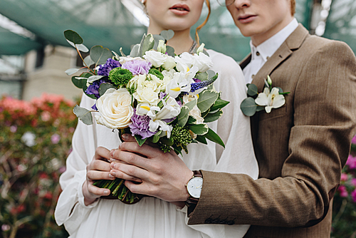 cropped shot of stylish young couple holding beautiful wedding bouquet