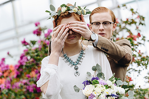 young man in eyeglasses closing eyes to beautiful redhead bride with wedding bouquet