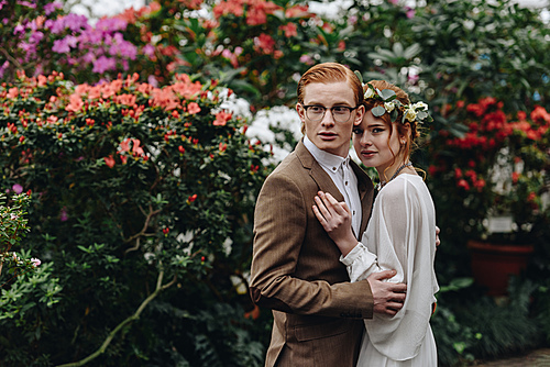 beautiful young elegant wedding couple standing together between flowers