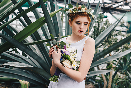 beautiful tender young redhead bride holding wedding bouquet in botanical garden