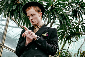 portrait of stylish young red hair man in hat in glasshouse