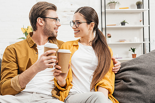young happy couple flirting and clinking paper cups of coffee on couch