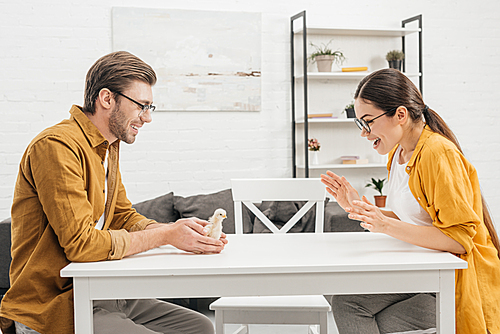 young man presenting little chick to surprised girlfriend on table at home