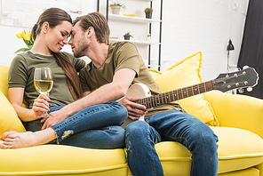 man cuddling with girlfriend while she holding glass of wine on couch at home