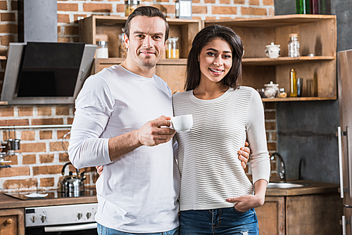 happy multiethnic couple smiling at camera while standing together in kitchen