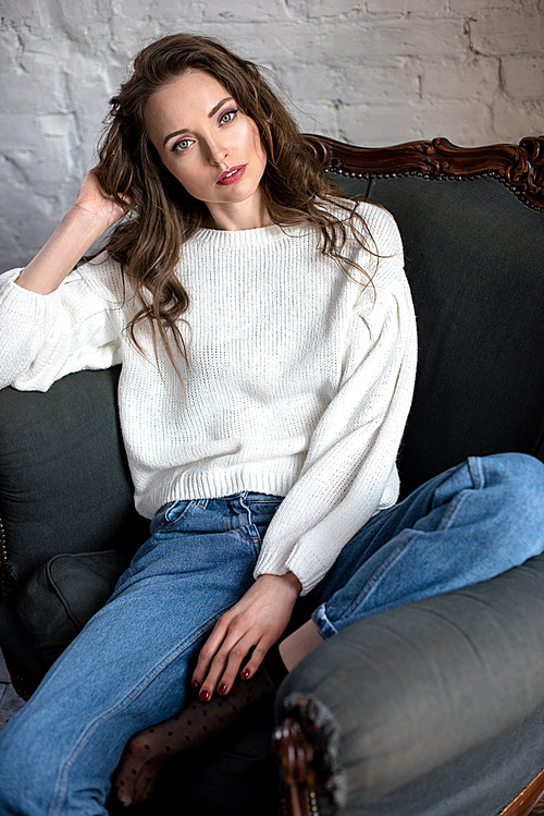 high angle view of sensual young woman in jumper and jeans sitting on armchair and