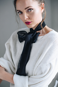 portrait of sensual young woman with black bow on neck  on grey