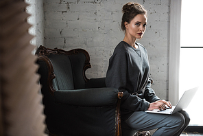 beautiful young woman using laptop and  while sitting on armchair