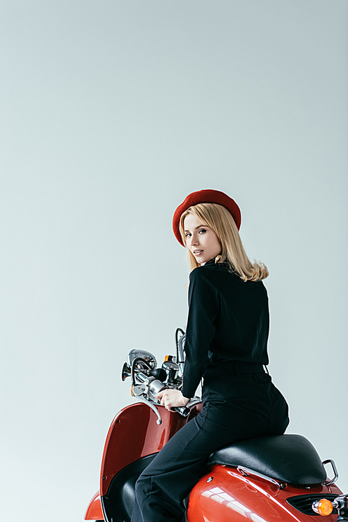 Stylish pretty woman standing by red scooter isolated on grey