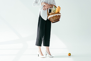 Close-up view of fashionable woman carrying basket with bread and flowers