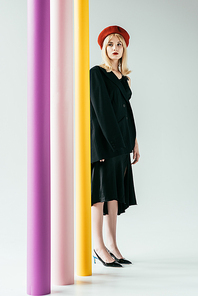 Stylish blonde girl in black dress posing by colorful pillars